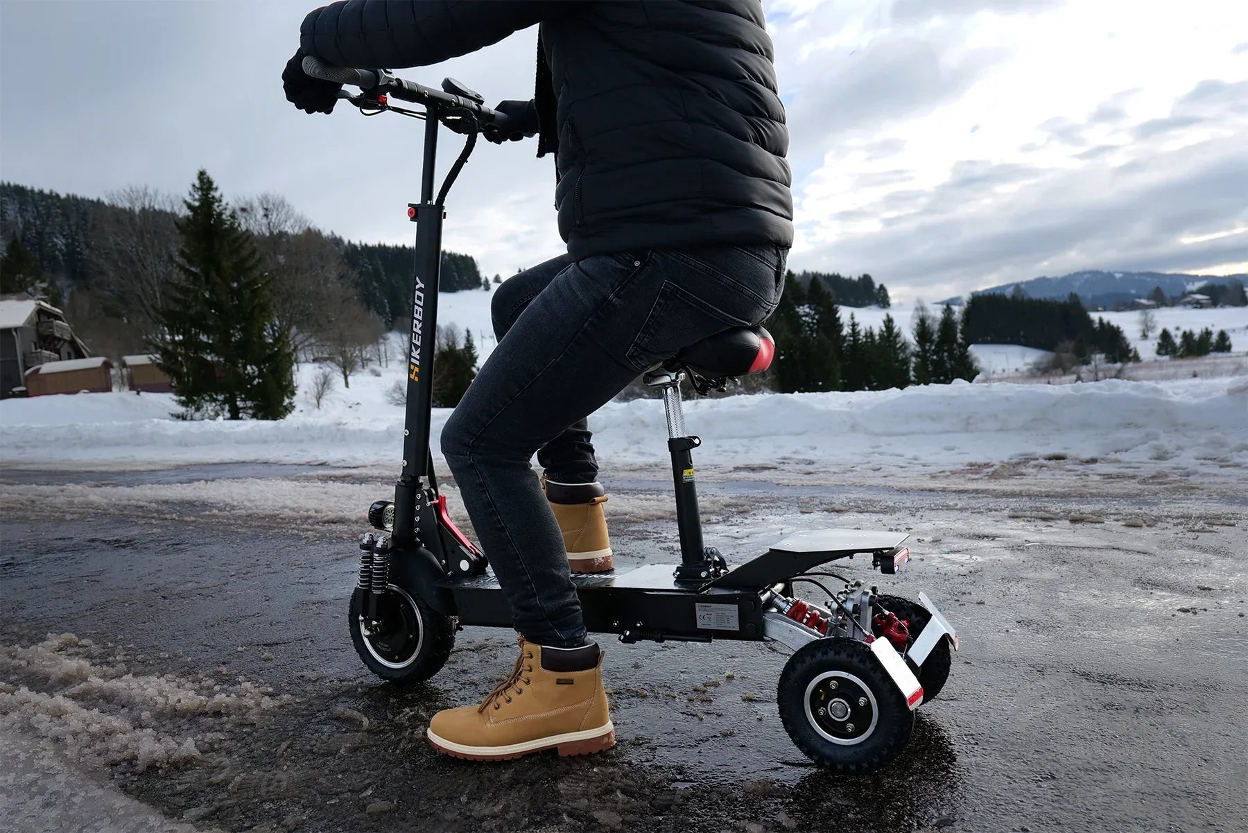 Person riding a scooter on a snowy landscape with trees and mountains in the background