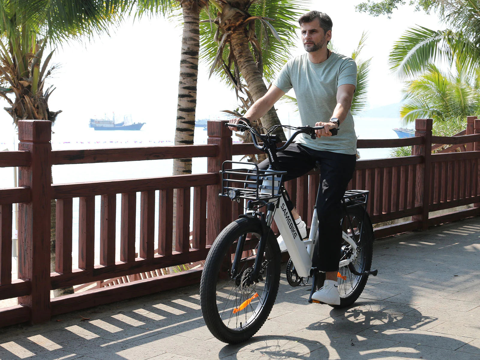 Man riding Samebike RS-A01 Plus Electric Bikeon a path with palm trees and a body of water in the background