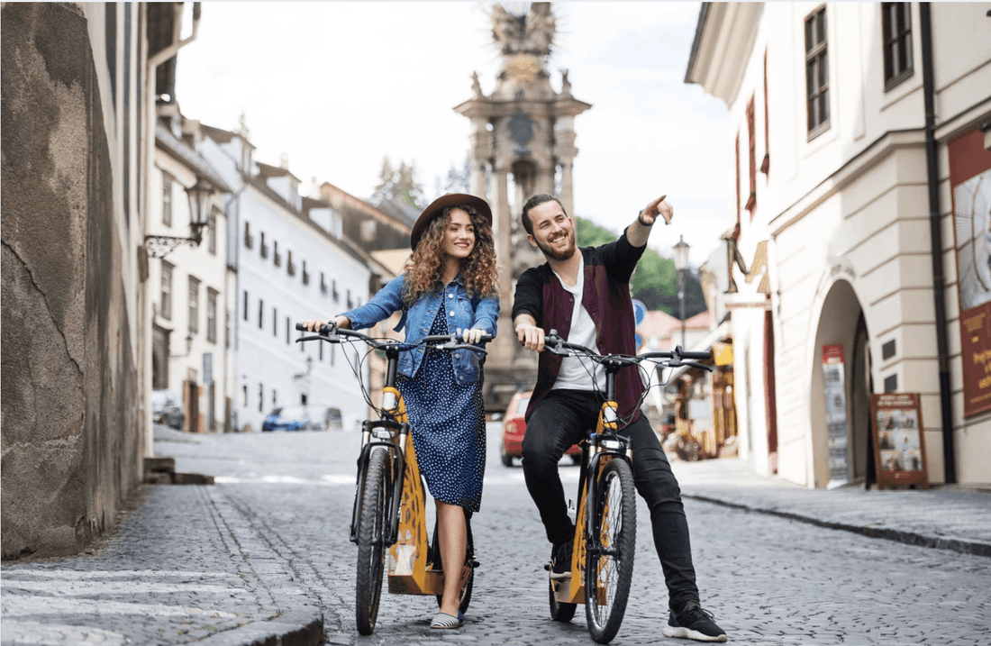 Young couple riding electric bikes in a European city street, enjoying Pogo Cycles e bikes
