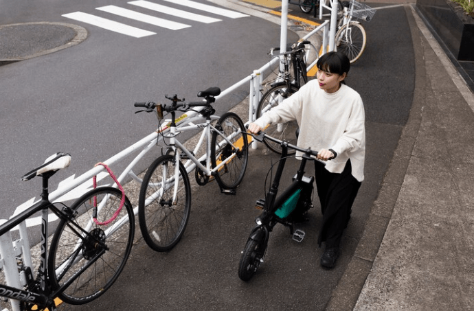 Woman walking an electric bike on urban sidewalk near other bicycles, Pogo Cycles e bikes