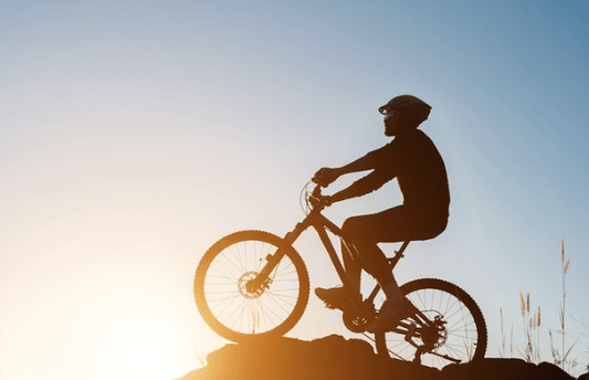 Silhouette of a cyclist riding an electric bike uphill at sunset, Pogo Cycles e-bike store
