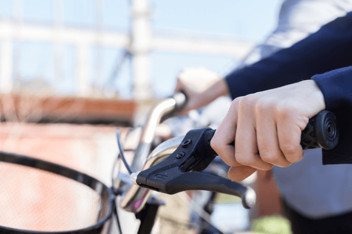 Close-up of electric bike handlebar and brake lever held by rider outdoors
