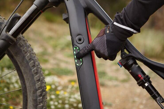 Close-up of electric mountain bike battery indicator being pressed, black and red frame
