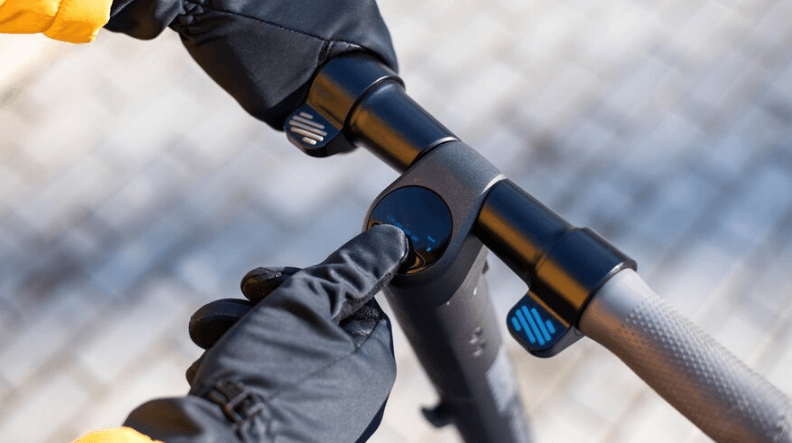 Gloved hand pressing power button on electric scooter handlebar, Pogo Cycles e bike store