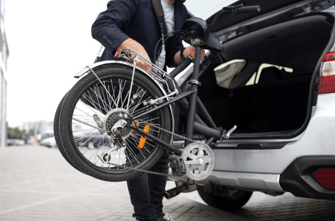 Man loading folding electric bike into car trunk, showcasing compact e-bike for commuting from Pogo Cycles